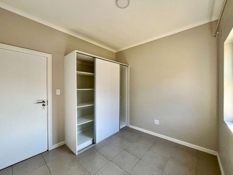 A clean, neutral bedroom featuring tiled flooring and a functional built-in wardrobe with sliding doors.