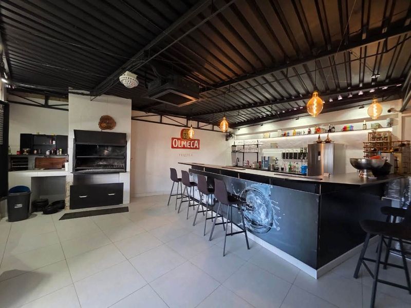A well-appointed entertainment bar area featuring a built-in bar counter, integrated braai, and modern industrial-style exposed ceiling finishes.