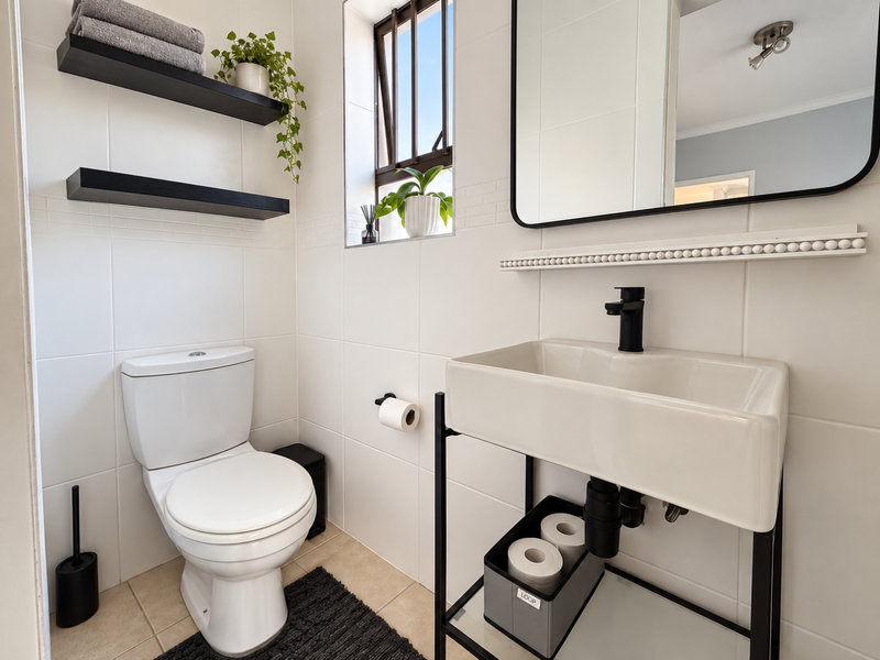 Modern bathroom featuring a wall-mounted toilet, a sleek ceramic basin with a black faucet on a metal vanity frame, and contemporary tiled finishes.