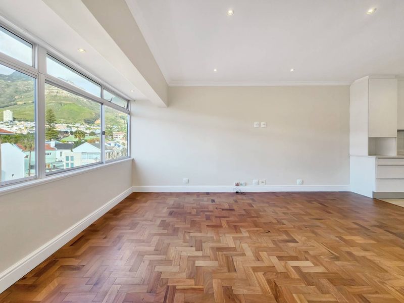 Spacious open-plan living area featuring classic herringbone parquet flooring, recessed lighting, and large windows offering scenic mountain views.