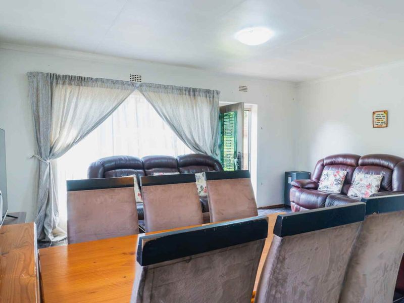 An open-plan living and dining area featuring neutral walls, large windows with curtains, and a functional layout suitable for family living.