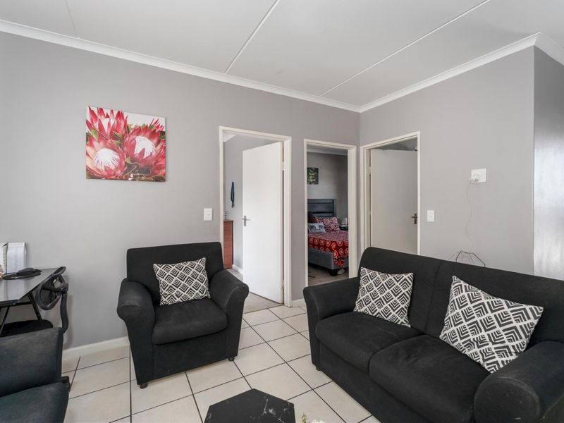 A living room featuring neutral grey walls, tiled flooring, and access to adjacent bedrooms through internal doorways.