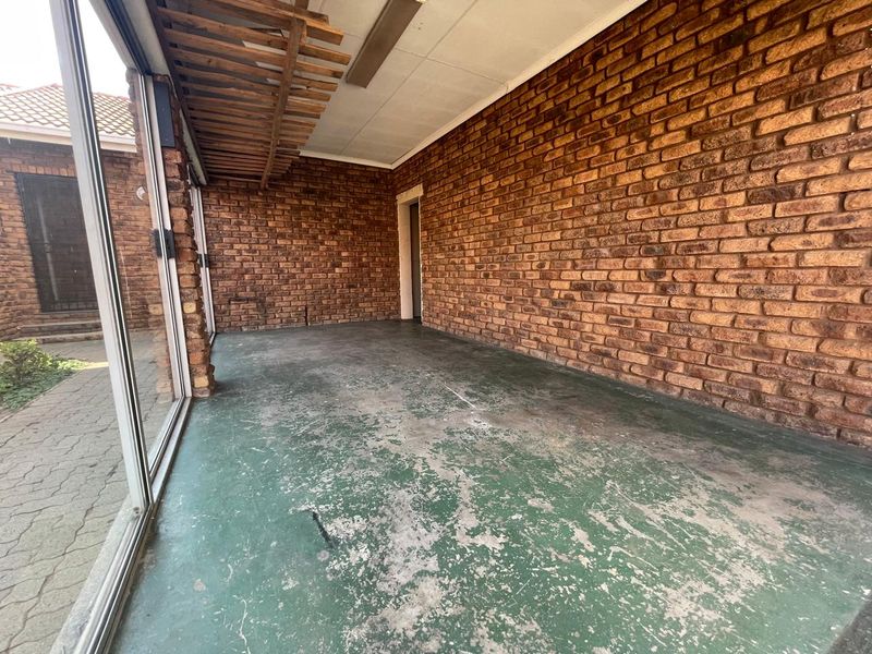 An outdoor patio area featuring exposed brick walls, a timber pergola, and sliding glass doors, currently requiring floor and ceiling maintenance.