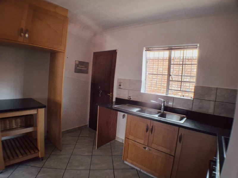 A functional kitchen featuring wooden cabinetry, stone countertops, a double bowl sink, and tiled flooring, currently vacant and ready for updates.