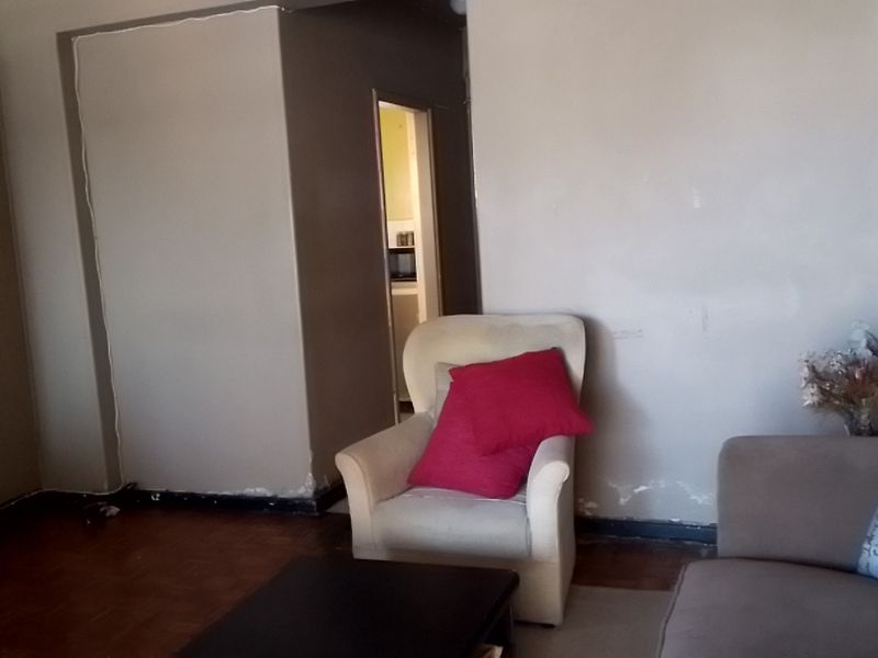 A living room area featuring parquet flooring and a built-in cupboard, showing signs of wear on the lower wall sections.