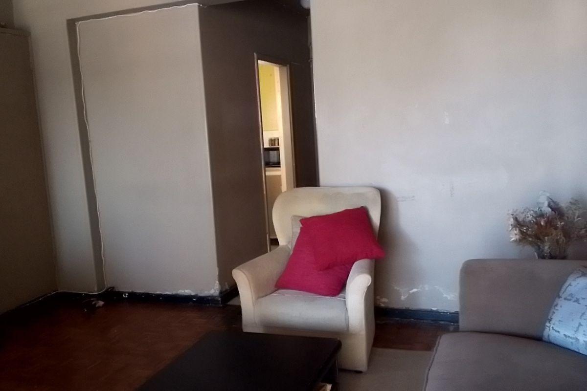 A living room area featuring parquet flooring and a built-in cupboard, showing signs of wear on the lower wall sections.