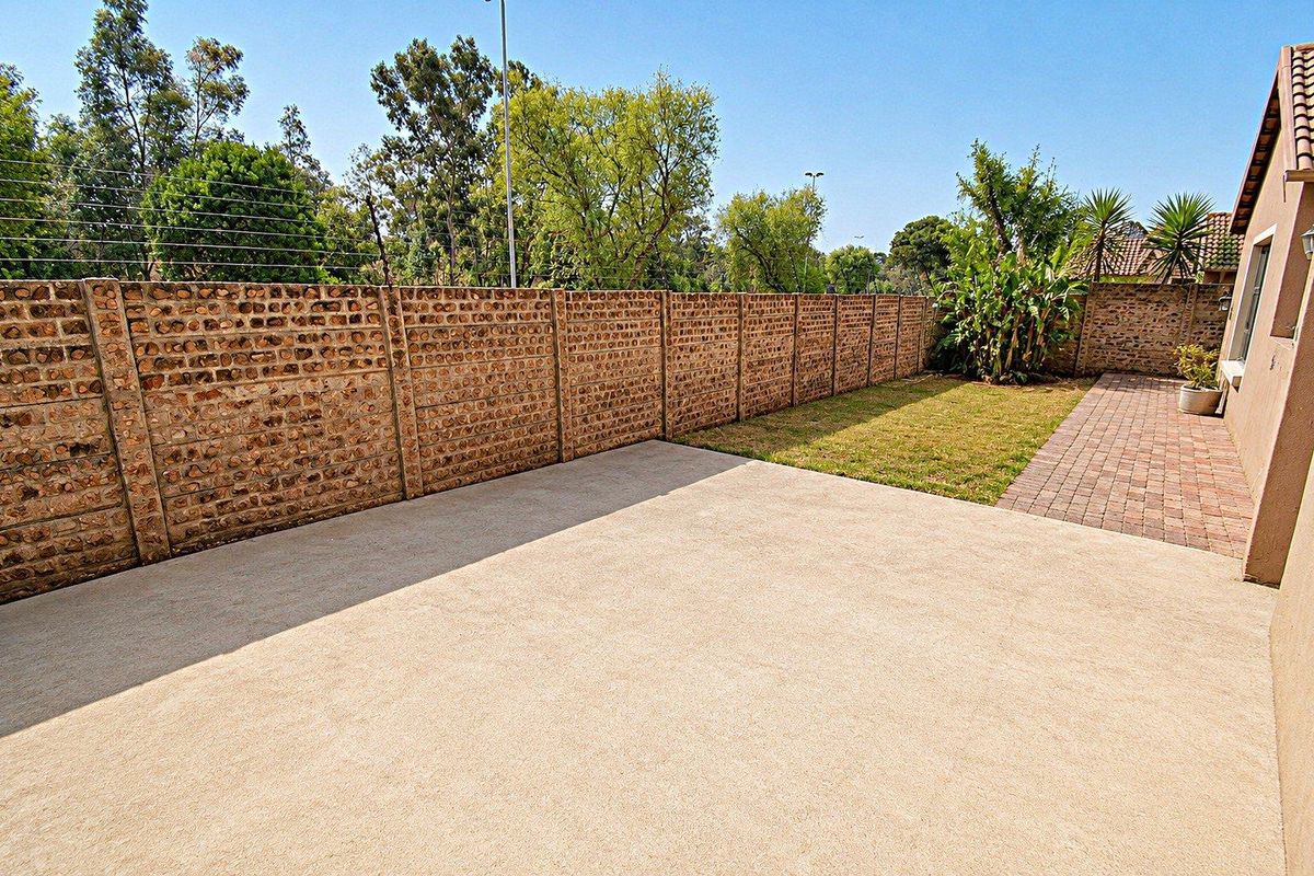 A private rear garden featuring a concrete patio, paved walkway, and a secure perimeter wall with electric fencing.