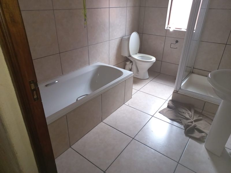 A functional bathroom featuring a bathtub, separate shower enclosure, toilet, and pedestal basin with neutral ceramic tiling throughout.