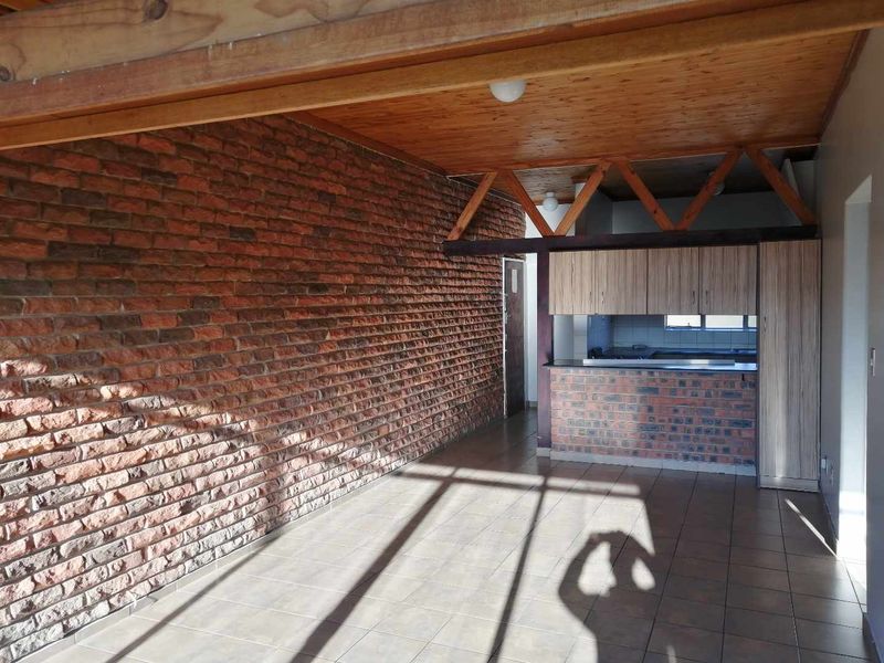 Open plan living area featuring exposed brick walls, timber ceiling beams, tiled floors, and a built-in kitchen breakfast bar.