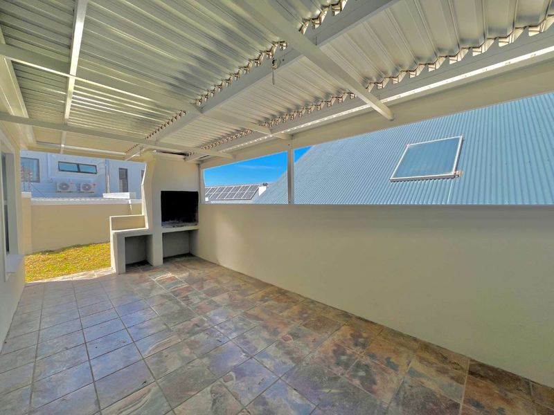 Covered outdoor patio featuring a built-in braai, tiled flooring, and a corrugated metal roof, providing a functional space for outdoor entertaining.