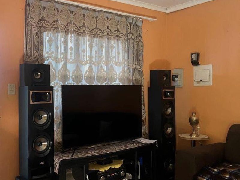 A living room area featuring tiled flooring and a ceiling rose, currently showing signs of wear and dated wall finishes.