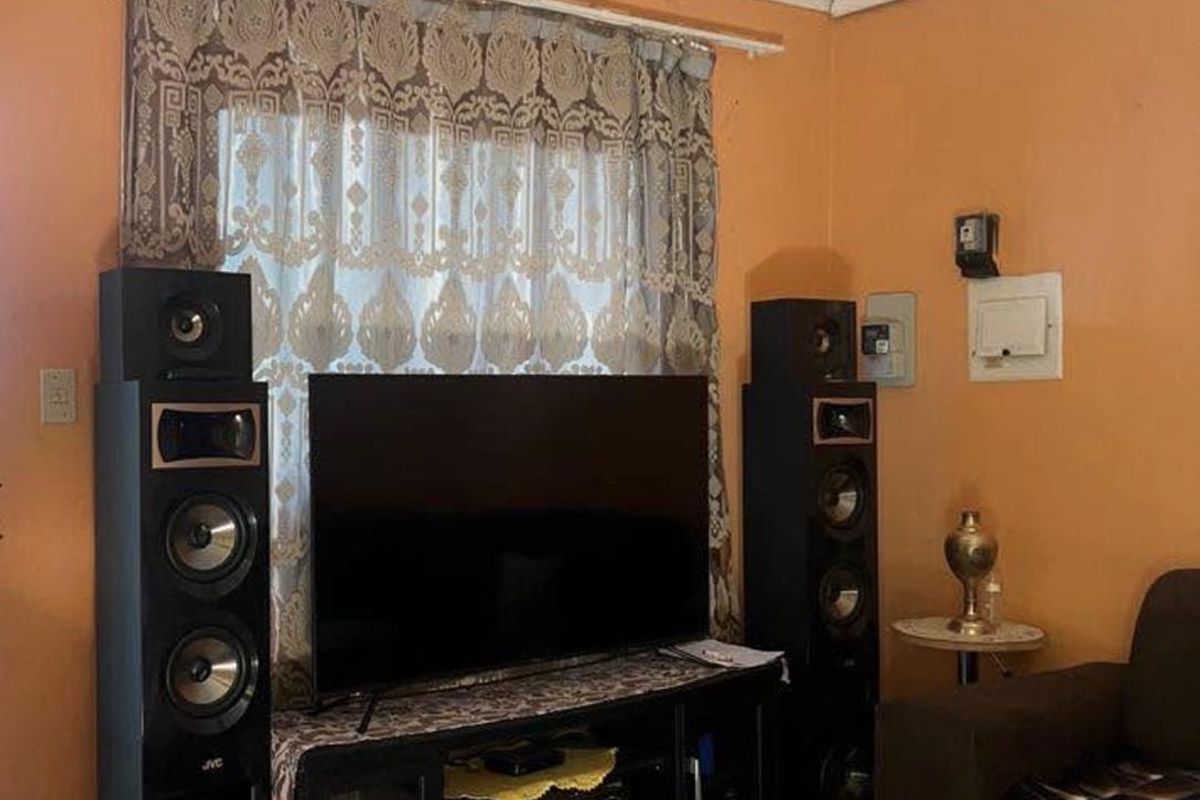 A living room area featuring tiled flooring and a ceiling rose, currently showing signs of wear and dated wall finishes.