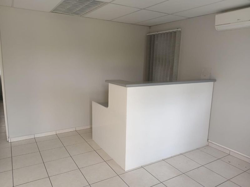 A clean, empty office space featuring a built-in reception desk, tiled flooring, drop ceiling, and a wall-mounted air conditioning unit.