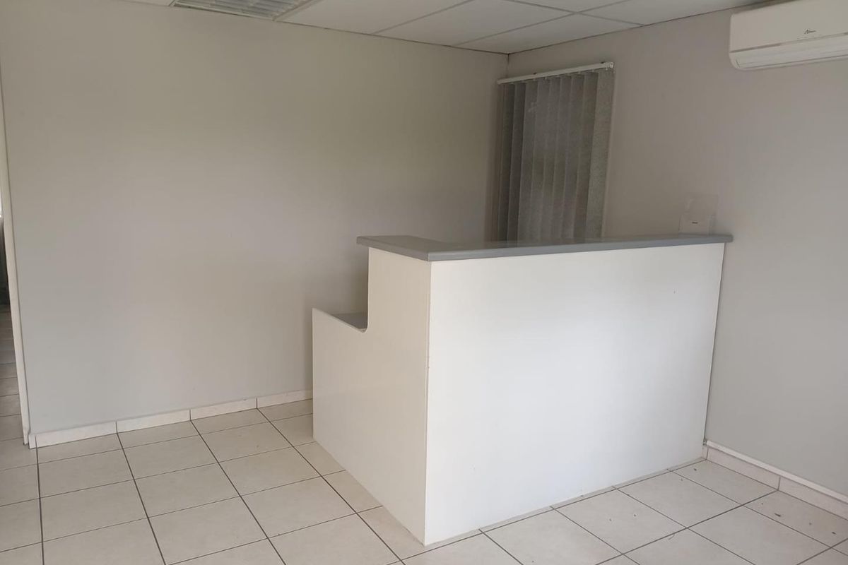 A clean, empty office space featuring a built-in reception desk, tiled flooring, drop ceiling, and a wall-mounted air conditioning unit.