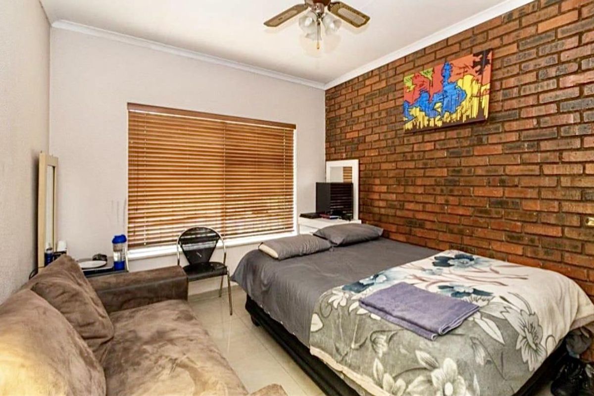 A bedroom featuring a prominent exposed brick feature wall, tiled flooring, and a ceiling fan.