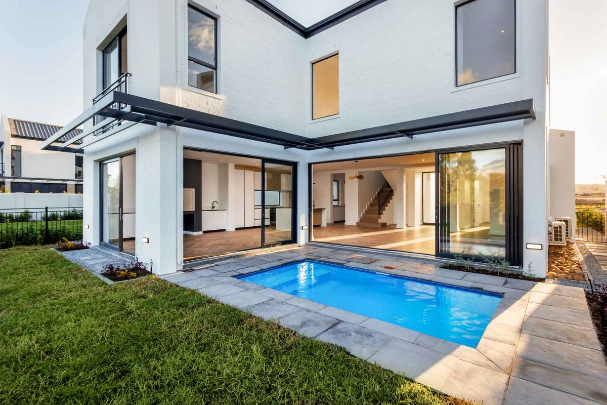 Modern rear exterior featuring a swimming pool, stone patio, and large sliding glass doors providing seamless indoor-outdoor flow to the open-plan living area.
