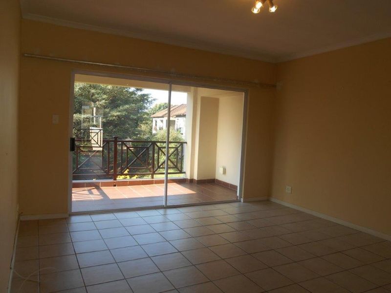An empty living room featuring tiled flooring and a large sliding glass door that opens onto a private balcony.