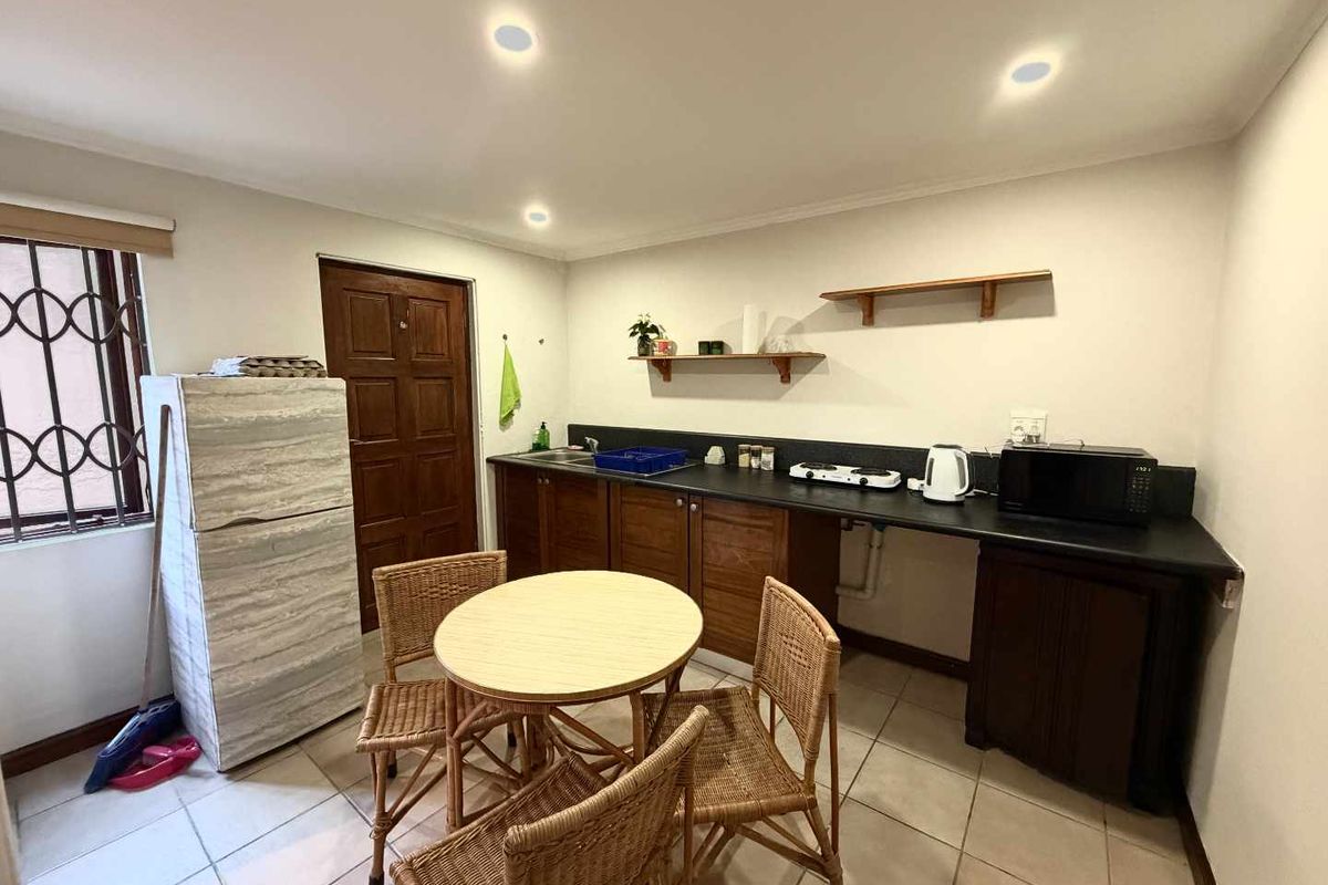 A functional kitchen area featuring dark wood cabinetry, black countertops, tiled flooring, and recessed lighting, with an adjacent dining space.