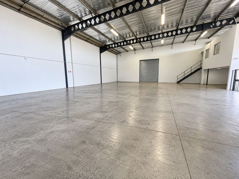 Spacious industrial warehouse unit featuring polished concrete floors, high-clearance steel truss roofing, a large roller shutter door, and an internal mezzanine staircase.