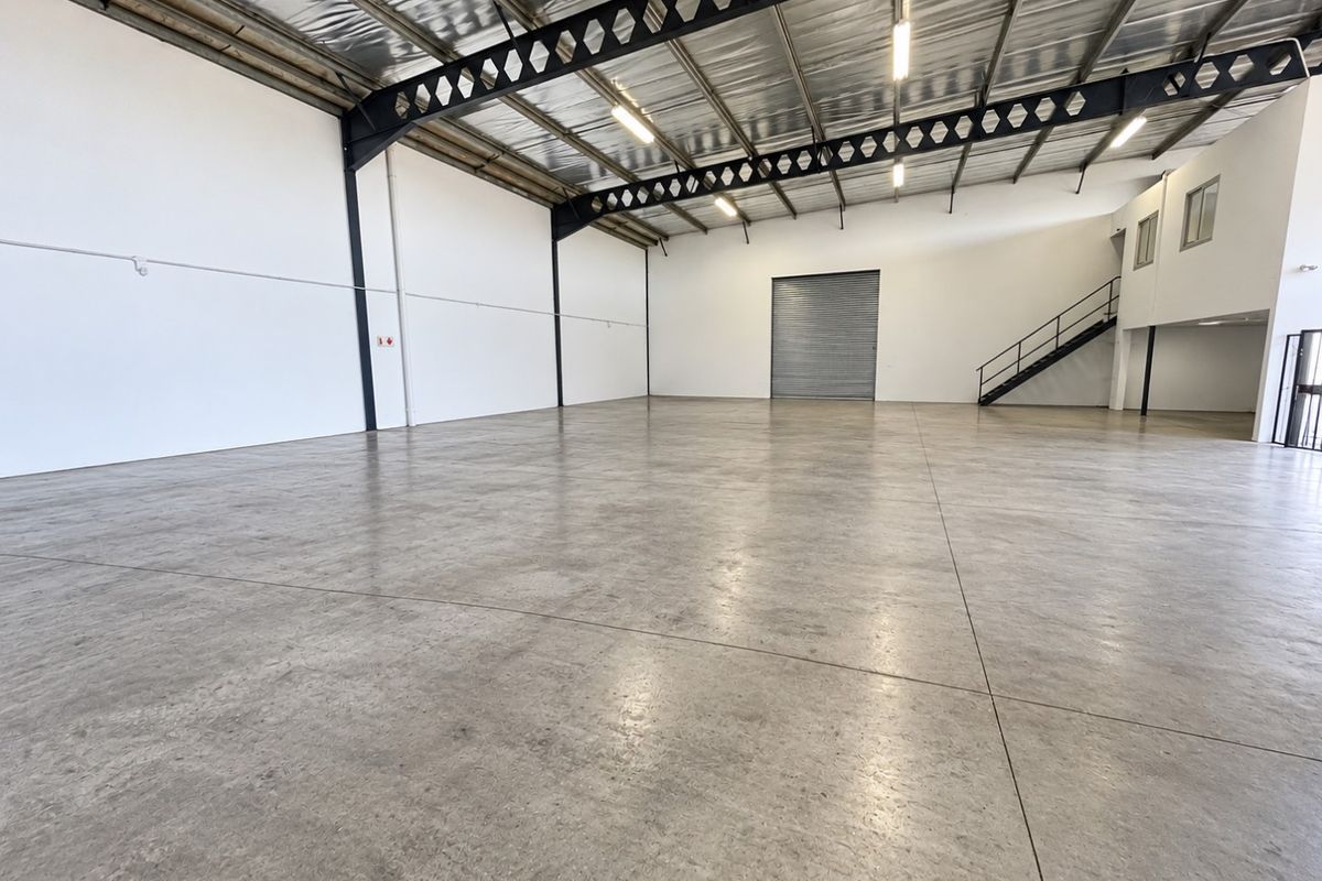 Spacious industrial warehouse unit featuring polished concrete floors, high-clearance steel truss roofing, a large roller shutter door, and an internal mezzanine staircase.