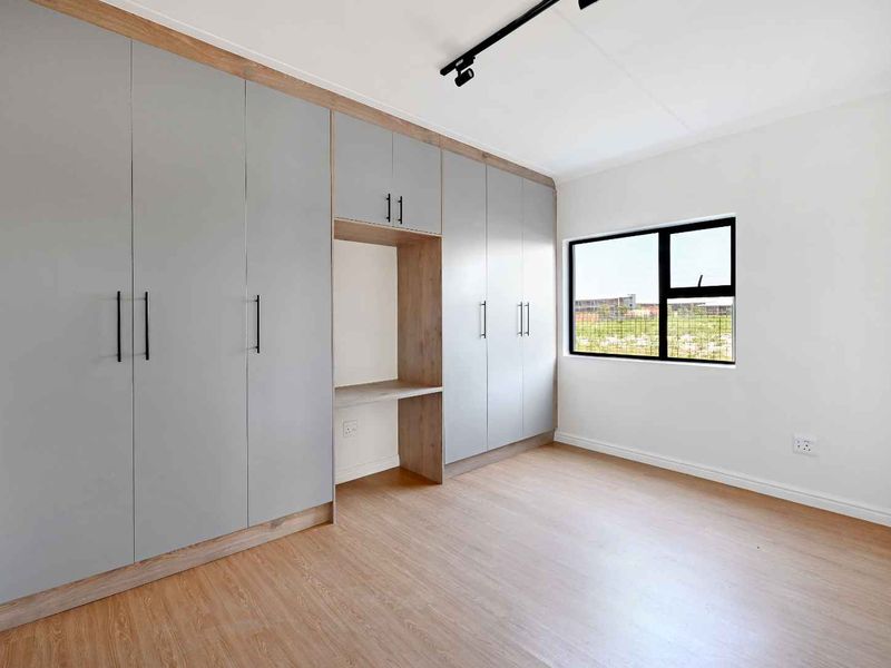A bright, modern bedroom featuring extensive built-in cabinetry with a integrated desk area, laminate flooring, and contemporary track lighting.