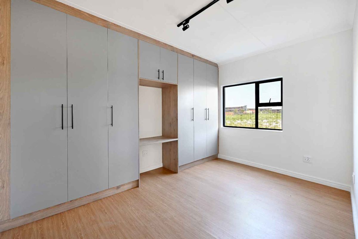 A bright, modern bedroom featuring extensive built-in cabinetry with a integrated desk area, laminate flooring, and contemporary track lighting.