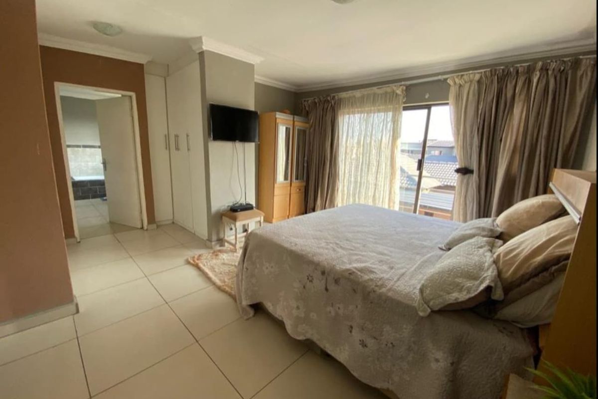 Spacious bedroom featuring tiled flooring, built-in cupboards, and sliding glass doors leading to an outdoor area, with an adjoining bathroom visible.
