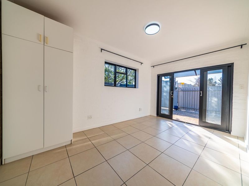 A bright, empty bedroom featuring tiled flooring, a built-in wardrobe, and sliding glass doors providing direct access to the outdoor area.