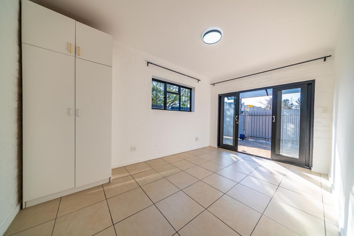 A bright, empty bedroom featuring tiled flooring, a built-in wardrobe, and sliding glass doors providing direct access to the outdoor area.
