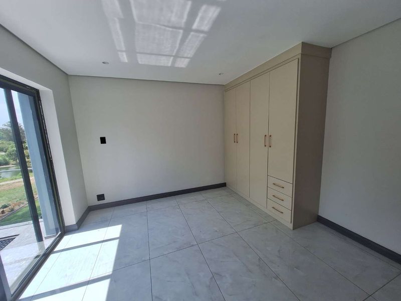 A bright, modern bedroom featuring neutral tiled flooring, built-in cupboards, and a large sliding glass door providing natural light and garden access.