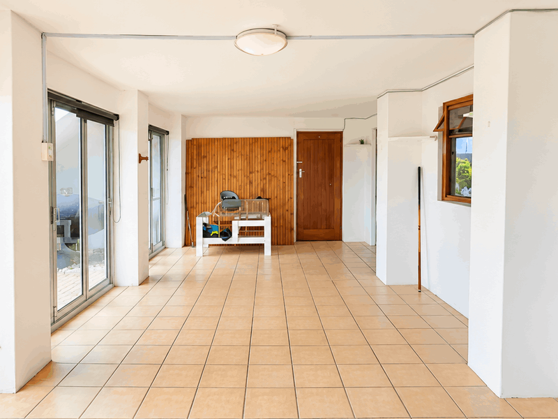 A spacious, covered patio area featuring tiled flooring, timber wall accents, and large sliding glass doors providing direct access to the garden.