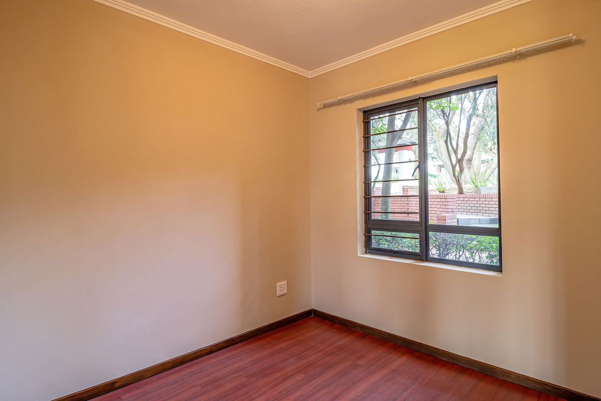 A bright, empty bedroom featuring laminate flooring, neutral walls, and a window fitted with security bars.