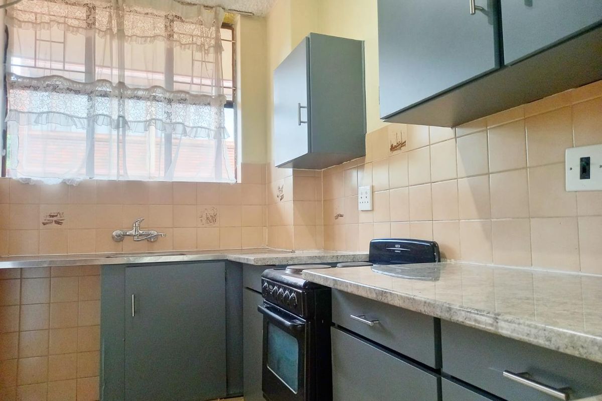 A functional kitchen featuring grey cabinetry, laminate countertops, a stainless steel sink, and a freestanding stove with tiled splashbacks.