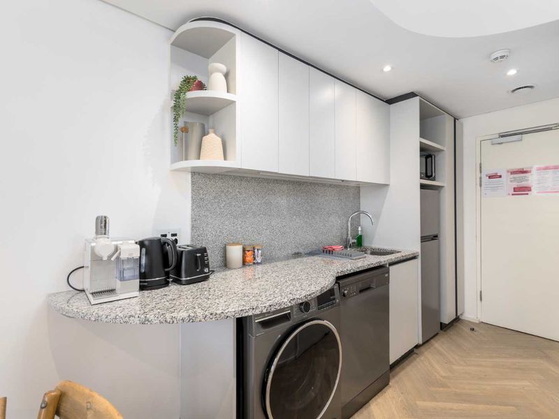Compact modern kitchen featuring granite countertops, integrated appliances including a dishwasher and washing machine, and stylish herringbone flooring.