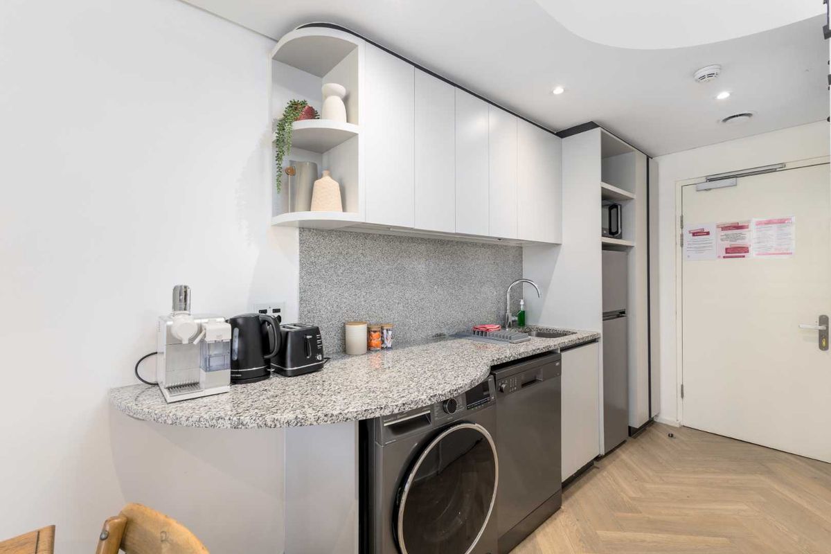 Compact modern kitchen featuring granite countertops, integrated appliances including a dishwasher and washing machine, and stylish herringbone flooring.
