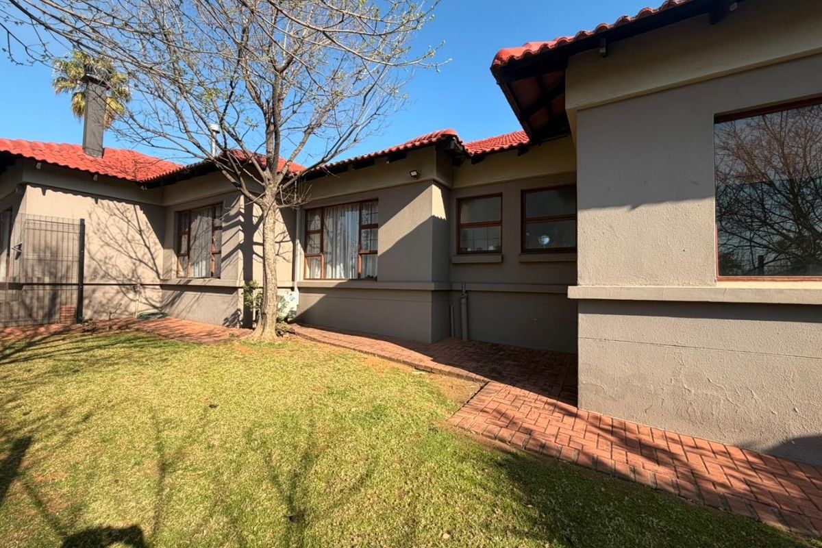 Rear view of the house featuring terracotta roof tiles, plastered walls, and a brick paved walkway leading along the garden.