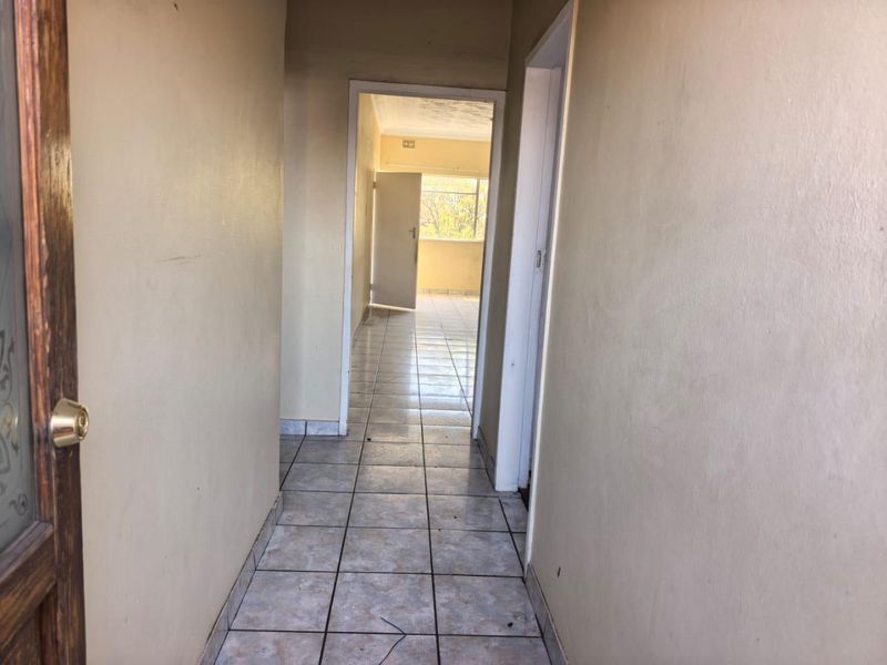 A vacant interior hallway featuring ceramic tiled flooring and neutral wall finishes, leading through to an adjacent room.
