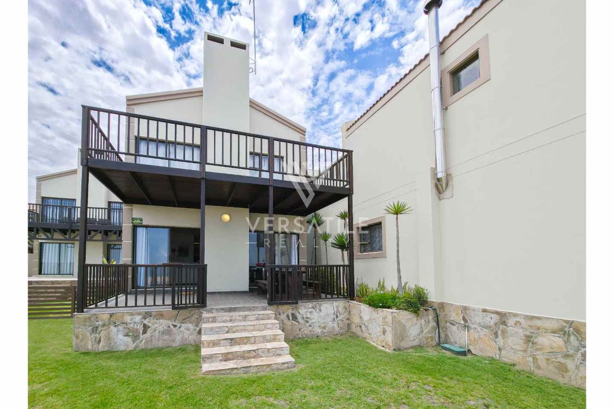 Rear view of the townhouse featuring a raised wooden balcony, stone-clad retaining wall, and a private garden area.