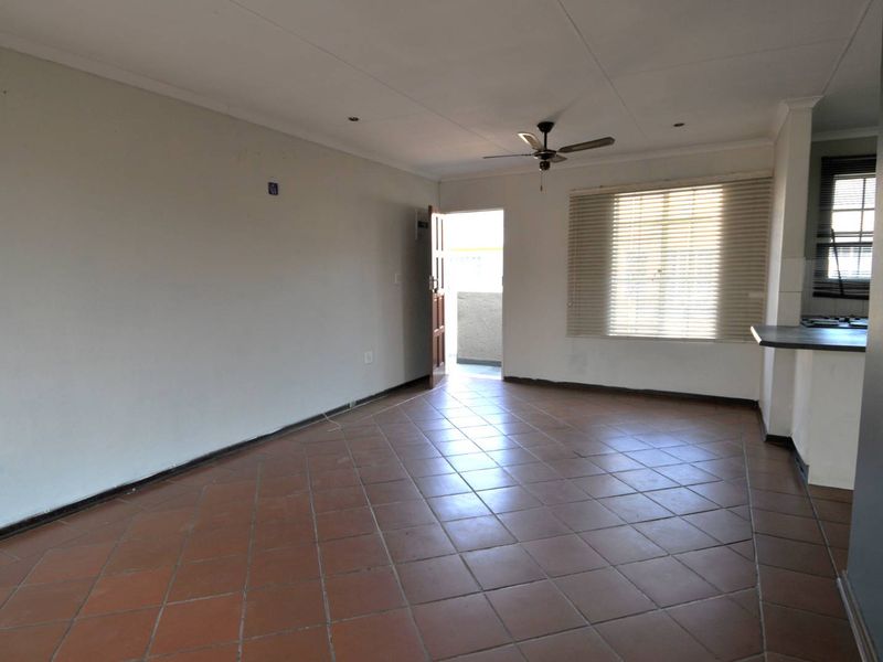 An open-plan living area featuring terracotta floor tiles, a ceiling fan, and a breakfast bar connecting to the kitchen space.