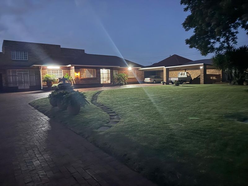 A well-maintained brick house exterior at dusk, featuring a spacious paved driveway, a covered carport, and a neatly landscaped front lawn.