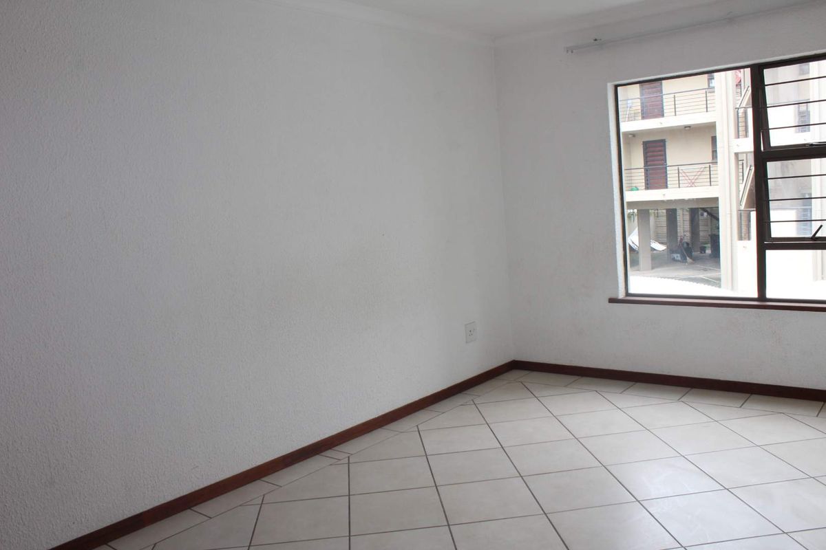 An empty bedroom featuring tiled flooring, white walls, and an aluminium window with security bars.