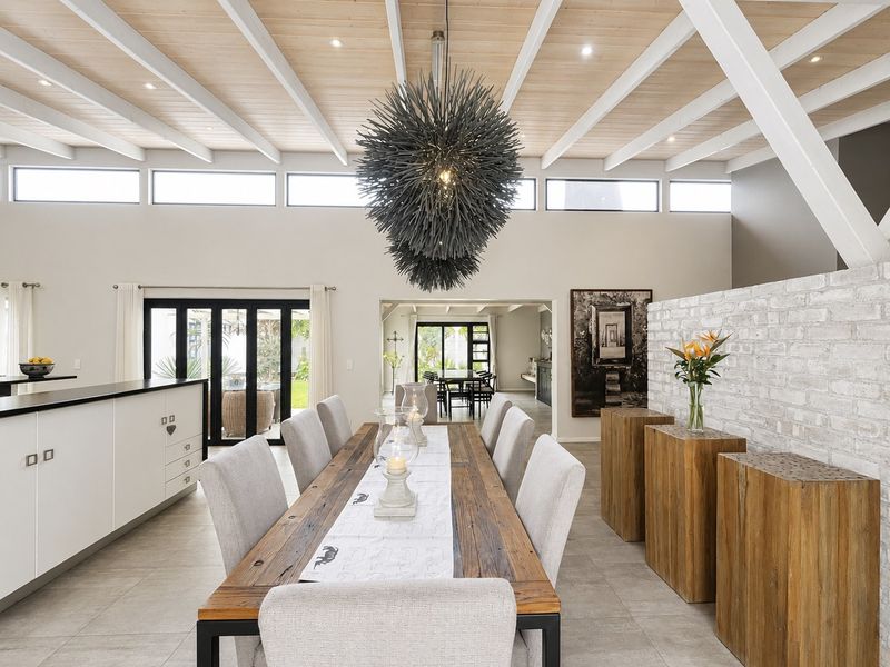 Spacious open-plan dining area featuring a high exposed beam ceiling, clerestory windows, and a striking white-painted brick feature wall with seamless indoor-outdoor flow.
