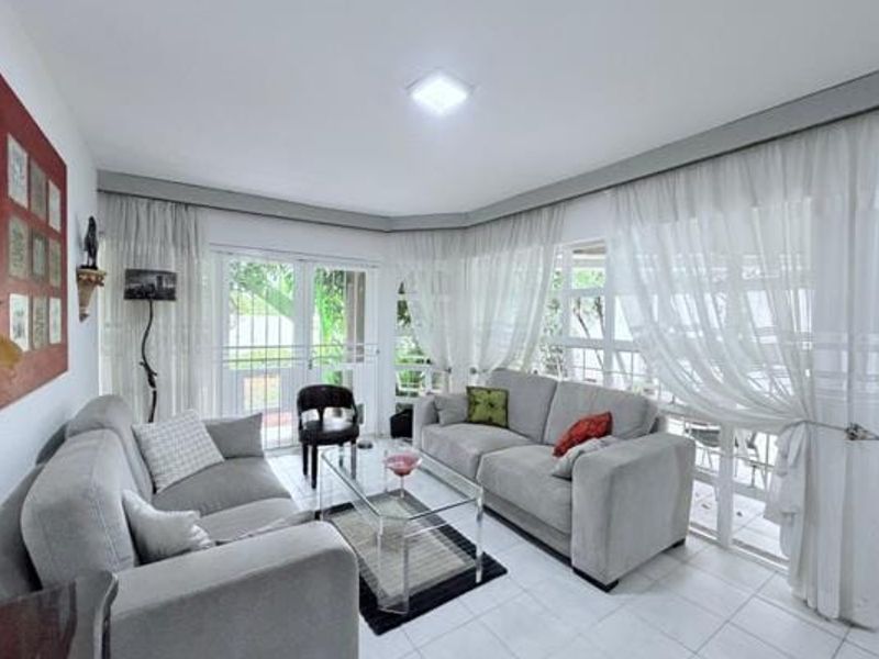A bright living room featuring tiled flooring, large sliding glass doors with security gates, and sheer curtains, providing direct access to the outdoor area.
