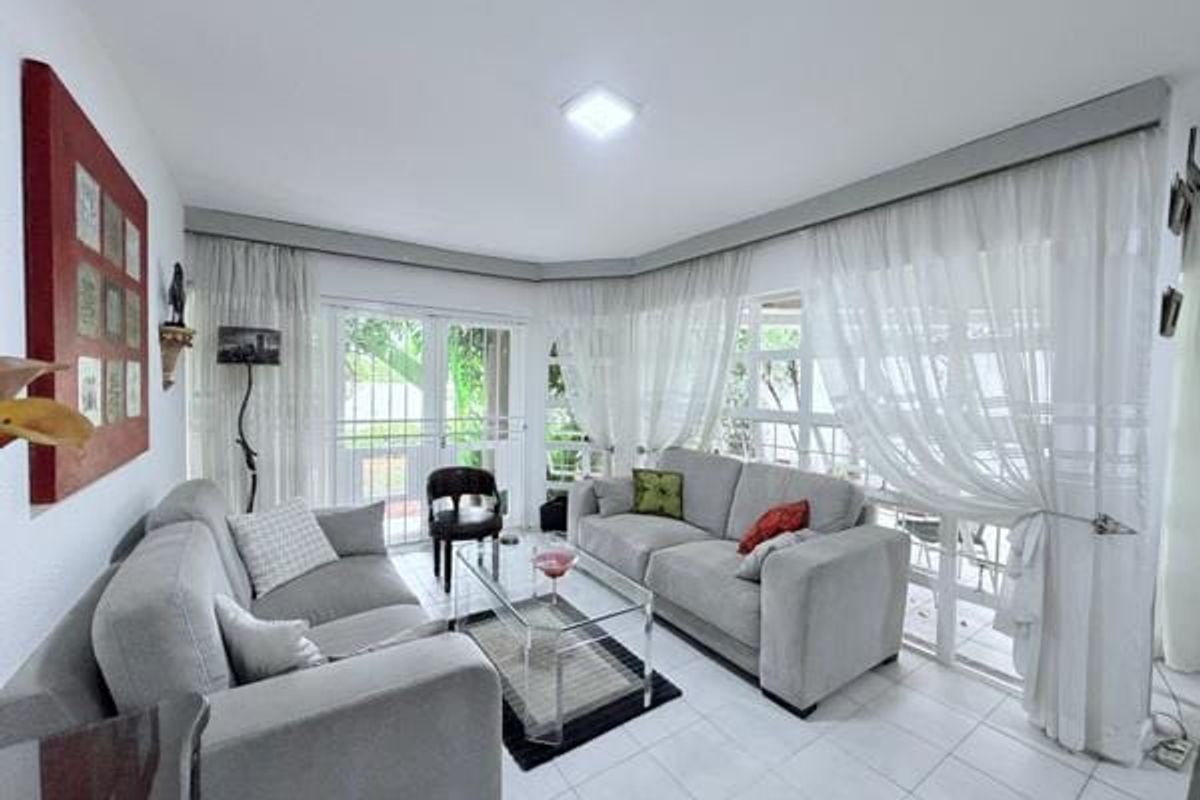 A bright living room featuring tiled flooring, large sliding glass doors with security gates, and sheer curtains, providing direct access to the outdoor area.