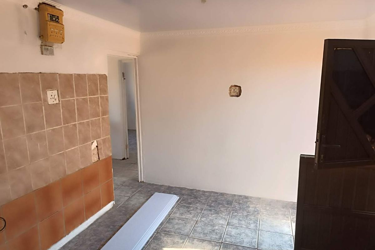 An empty kitchen area featuring tiled flooring, partial wall tiling, and visible electrical infrastructure, currently undergoing maintenance or renovation.