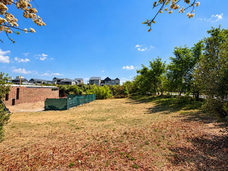 A view of a vacant residential plot featuring established trees and partial perimeter fencing, situated in a developed residential estate.