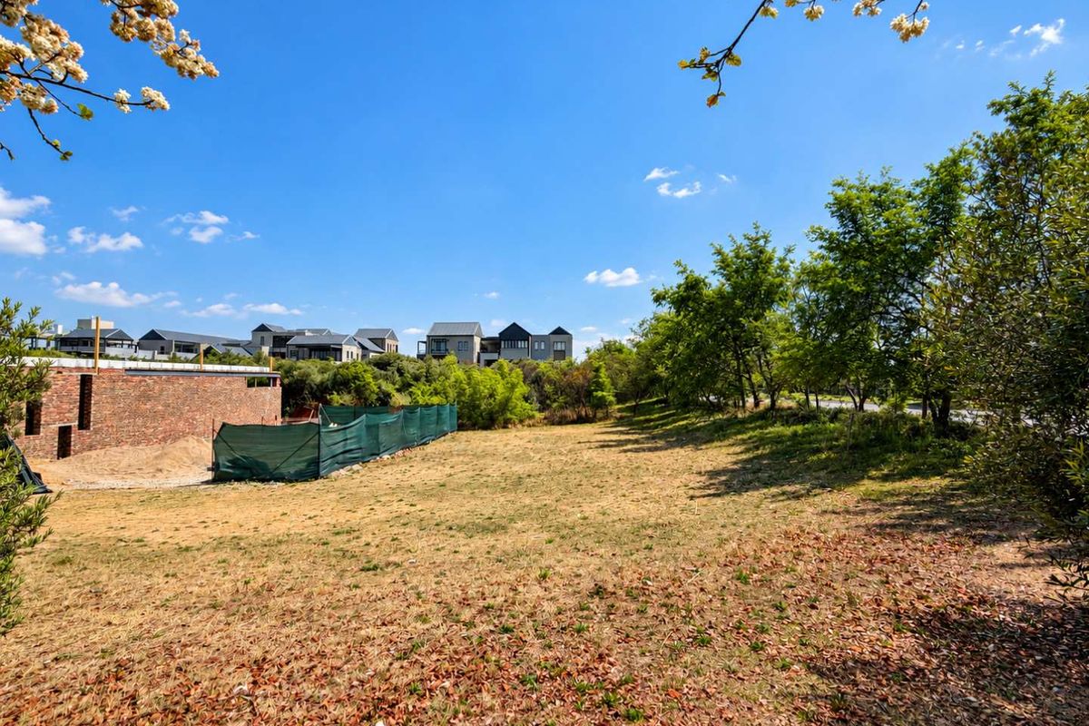 A view of a vacant residential plot featuring established trees and partial perimeter fencing, situated in a developed residential estate.
