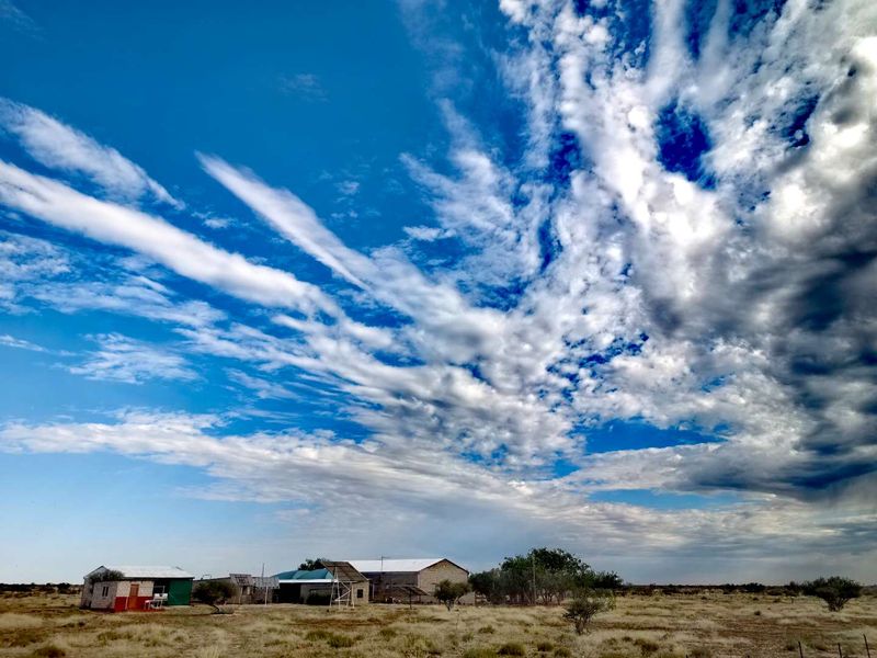 A wide-angle view of the farm property featuring multiple outbuildings with corrugated metal roofing set against a vast open landscape.