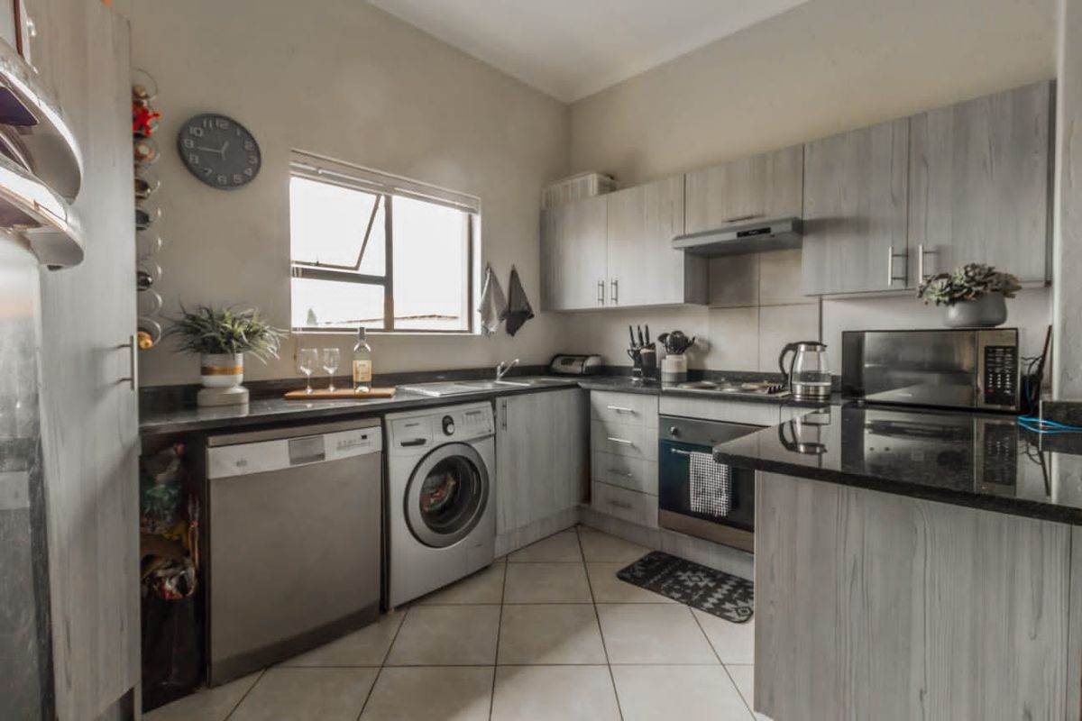 A functional kitchen featuring light wood-grain cabinetry, dark granite countertops, tiled flooring, and integrated stainless steel appliances including an oven and extractor fan.