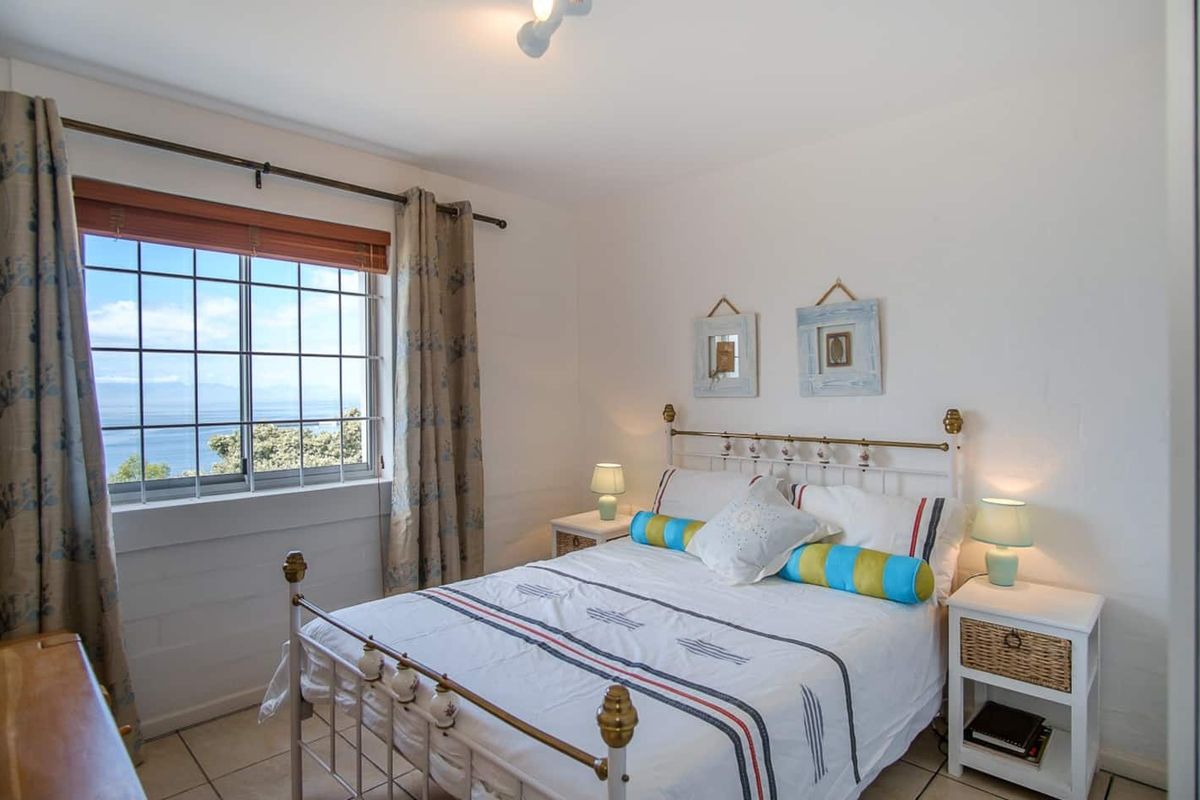 A bright bedroom featuring tiled flooring, a metal-framed bed, and a window offering scenic coastal views.
